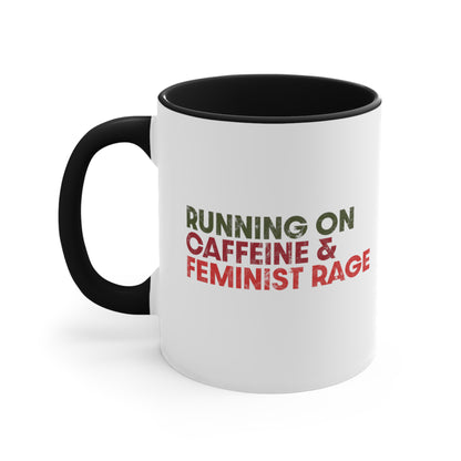 11oz ceramic mug with a black interior and handle color that says, “RUNNING ON CAFFEINE & FEMINIST RAGE” with each line being a different color. “RUNNING ON” is dark green, “CAFFEINE &” is dark red, and “FEMINIST RAGE” is dark orange. The text is slightly distressed.