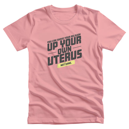 Pink unisex t-shirt that says, “You Can Shove Your Religion Up Your Own Uterus, Not Mine.” The text is all slanted upwards, and the words “Not Mine” are in a yellow rectangle.