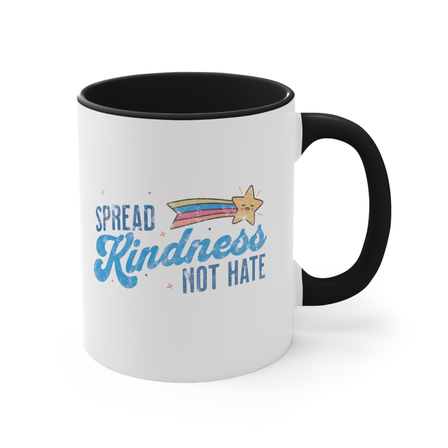 11oz ceramic mug with a black interior and handle. It has a graphic that says “Spread Kindness Not Hate” with an illustration of a rainbow shooting star over the word “kindness.” That word is in a script font, and the rest is a regular font in all caps. ”Spread” is on top of the word “Kindness” and aligned left, while “Not Hate” is below the word “kindness” and aligned to the right.