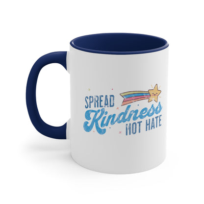 11oz ceramic mug with a navy blue interior and handle. It has a graphic that says “Spread Kindness Not Hate” with an illustration of a rainbow shooting star over the word “kindness.” That word is in a script font, and the rest is a regular font in all caps. ”Spread” is on top of the word “Kindness” and aligned left, while “Not Hate” is below the word “kindness” and aligned to the right.