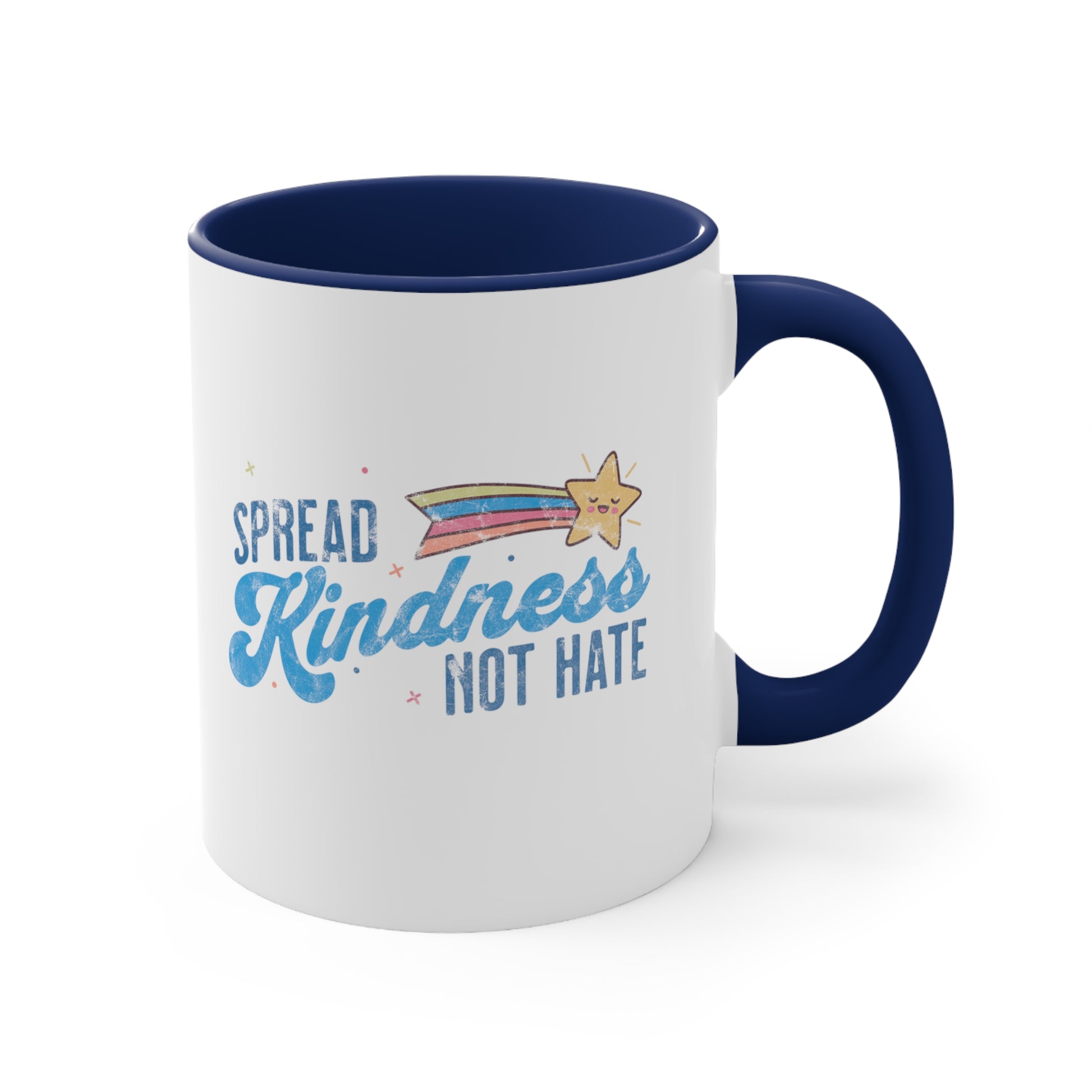 11oz ceramic mug with a navy blue interior and handle. It has a graphic that says “Spread Kindness Not Hate” with an illustration of a rainbow shooting star over the word “kindness.” That word is in a script font, and the rest is a regular font in all caps. ”Spread” is on top of the word “Kindness” and aligned left, while “Not Hate” is below the word “kindness” and aligned to the right.