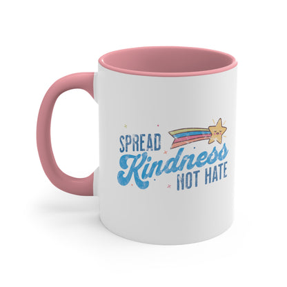 11oz ceramic mug with a pink interior and handle. It has a graphic that says “Spread Kindness Not Hate” with an illustration of a rainbow shooting star over the word “kindness.” That word is in a script font, and the rest is a regular font in all caps. ”Spread” is on top of the word “Kindness” and aligned left, while “Not Hate” is below the word “kindness” and aligned to the right.