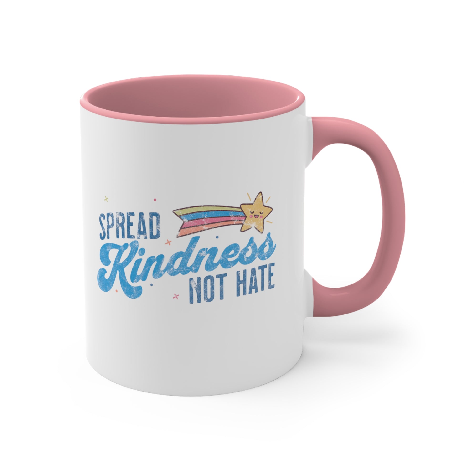 11oz ceramic mug with a pink interior and handle. It has a graphic that says “Spread Kindness Not Hate” with an illustration of a rainbow shooting star over the word “kindness.” That word is in a script font, and the rest is a regular font in all caps. ”Spread” is on top of the word “Kindness” and aligned left, while “Not Hate” is below the word “kindness” and aligned to the right.