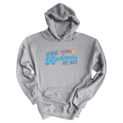 Sport Grey color unisex hoodie with a graphic that says “Spread Kindness Not Hate” with an illustration of a rainbow shooting star over the word “kindness.” That word is in a script font, and the rest is a regular font in all caps. ”Spread” is on top of the word “Kindness” and aligned left, while “Not Hate” is below the word “kindness” and aligned to the right.