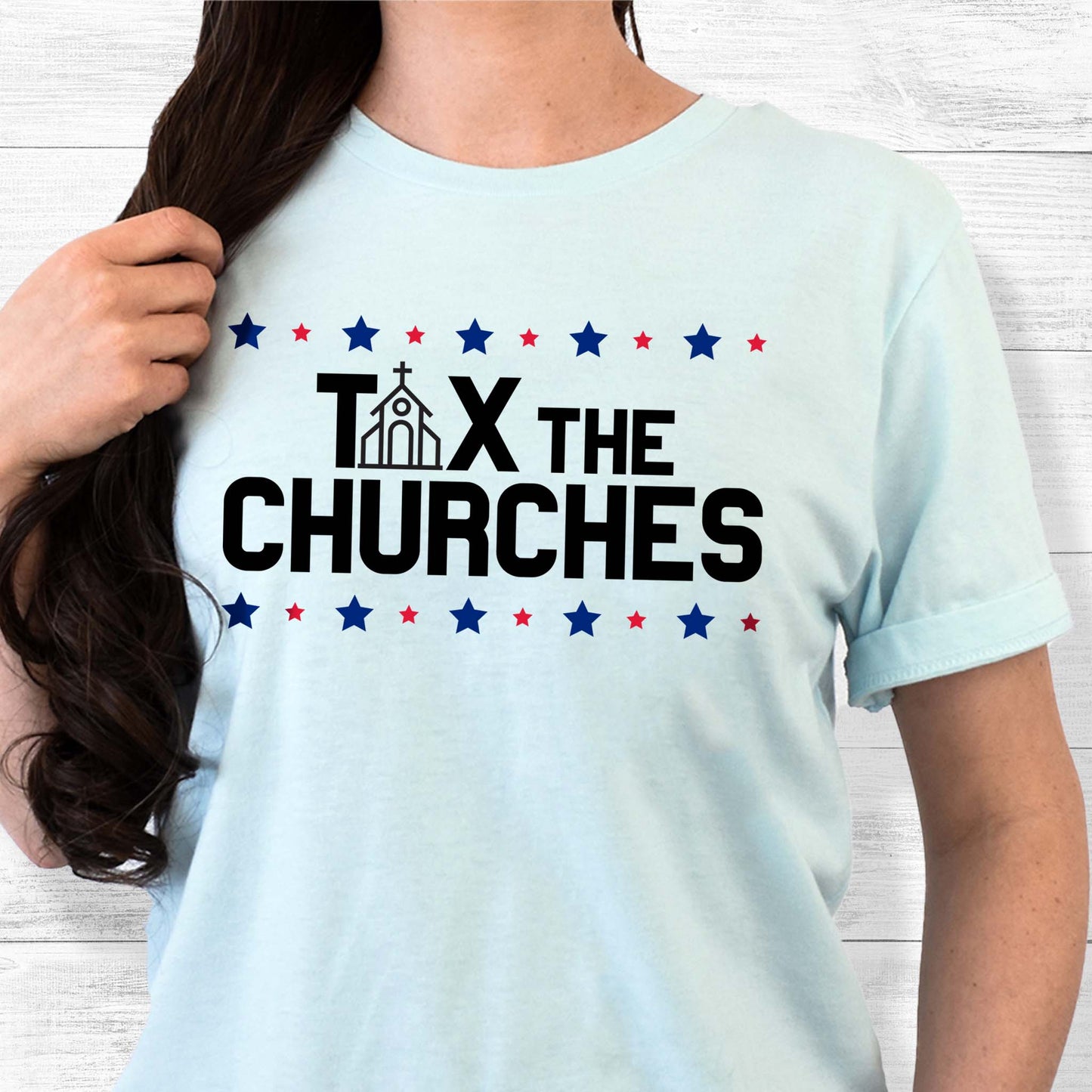 Heather Ice Blue color unisex t-shirt that says, “Tax the Churches” in all caps. There are alternating large and small stars in a line above and below the text. The “A” in “Tax” is a line illustration of a church.