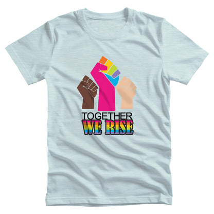 Heather Ice Blue color unisex t-shirt with a graphic a brown skin-colored fist on the left, a rainbow fist front and center, and a white skin-colored fist on the right. Below that reads “Together We Rise.” “Together” is on one line and “We Rise” is below that in rainbow colors.