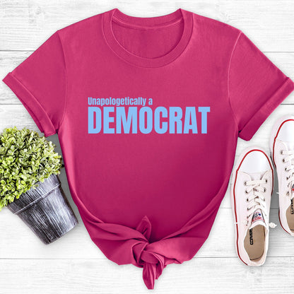 Berry color unisex t-shirt that says, “Unapologetically a Democrat” in all caps. The words “Unapologetically a” are a smaller font size on their own line. The word “Democrat” is beneath that and spans across the chest.