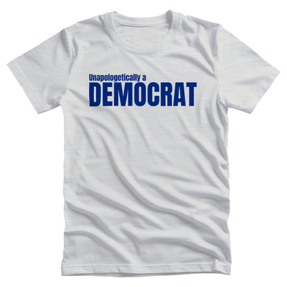 Ash color unisex t-shirt that says, “Unapologetically a Democrat” in all caps. The words “Unapologetically a” are a smaller font size on their own line. The word “Democrat” is beneath that and spans across the chest.