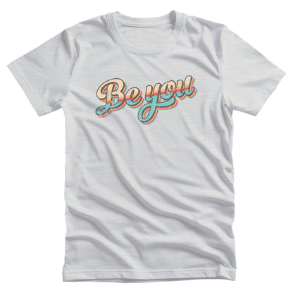 Ash color unisex t-shirt that says “Be you” in a vintage-inspired script font with vintage colors and stripes. It’s designed to look as if the design is wearing off the shirt.