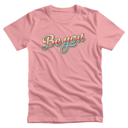 Pink unisex t-shirt that says “Be you” in a vintage-inspired script font with vintage colors and stripes. It’s designed to look as if the design is wearing off the shirt.