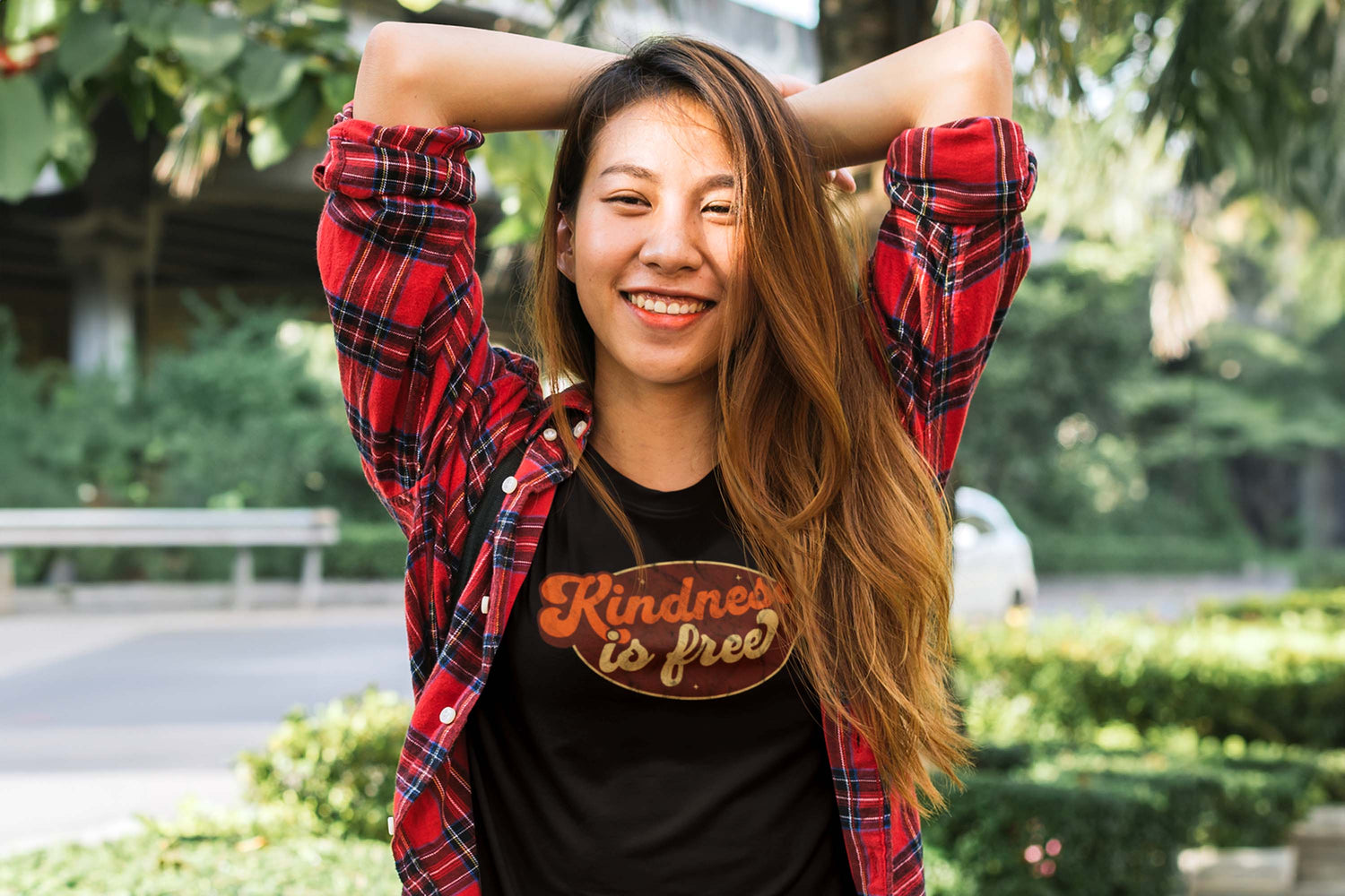 A woman wearing a shirt that says "Kindness is Free" in a script font in retro colors inside an oval.