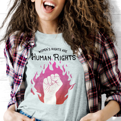 Heather Ice Blue color unisex t-shirt with a graphic of a fist over pink and red flames. The text says, “Women’s rights are human rights” with the words “women’s rights are” arched over the words “Human Rights”.