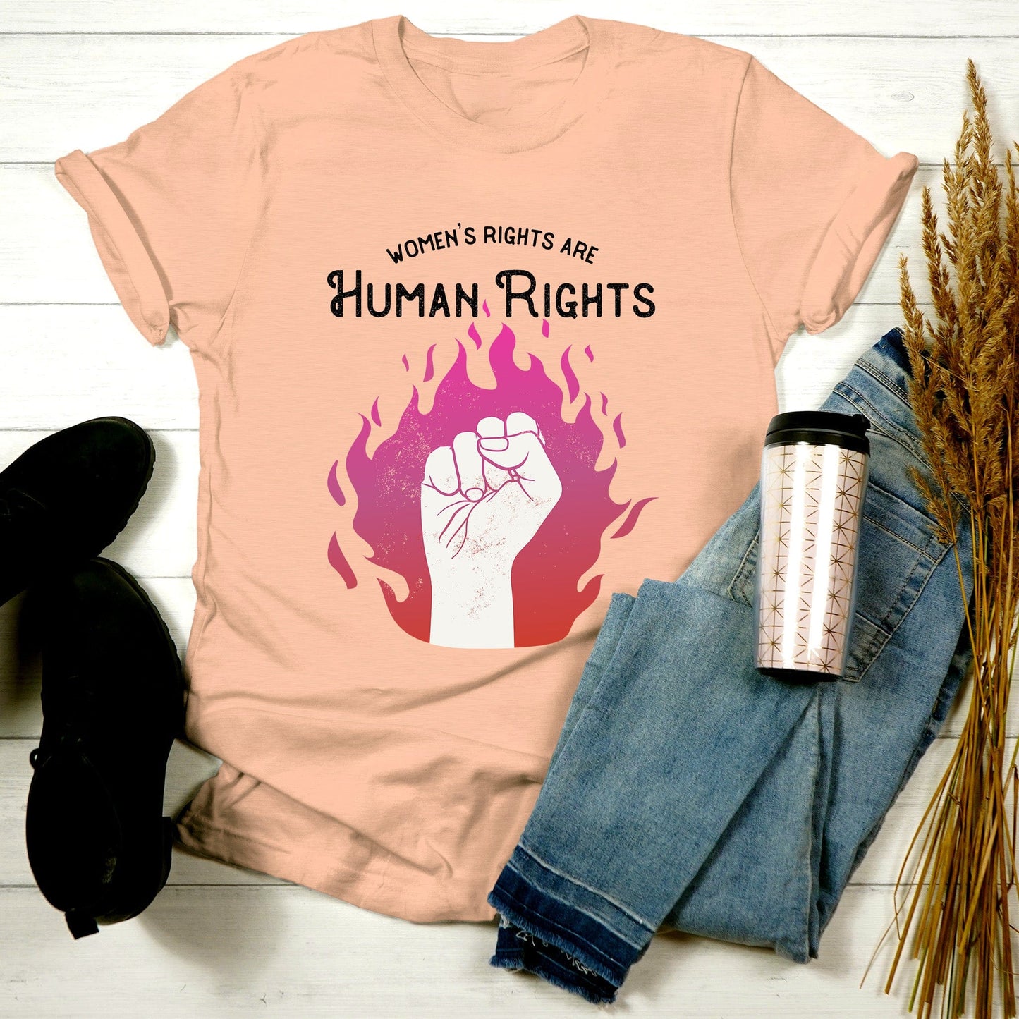 Heather Peach color unisex t-shirt with a graphic of a fist over pink and red flames. The text says, “Women’s rights are human rights” with the words “women’s rights are” arched over the words “Human Rights”.