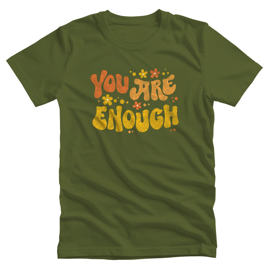 Olive color unisex t-shirt with a graphic that says “You Are Enough” in a retro font. There are small retro flowers spaced throughout. “You” is reddish-orange, “Are” is orange, and “Enough” is yellow, all retro as well.