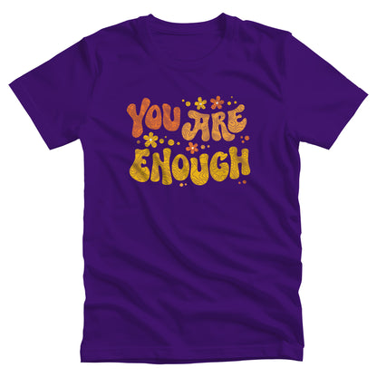 Team Purple color unisex t-shirt with a graphic that says “You Are Enough” in a retro font. There are small retro flowers spaced throughout. “You” is reddish-orange, “Are” is orange, and “Enough” is yellow, all retro as well.