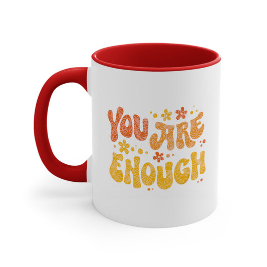 11oz ceramic mug with a red interior and handle. The graphic on it says “You Are Enough” in a retro font. There are small retro flowers spaced throughout. “You” is reddish-orange, “Are” is orange, and “Enough” is yellow, all retro as well.